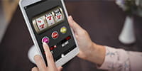 Zwei Händen halten ein Tablet und spielen ein Spielothekenpiel.