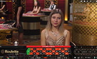 Ein weiblicher Live Dealer sitzt im Omni Slots Live Spielothek vor einem Roulettetisch.