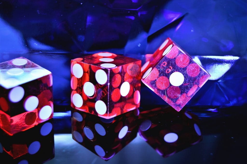 Drei rote Casino-Würfel auf spiegelndem Tisch in Schwarzlicht.