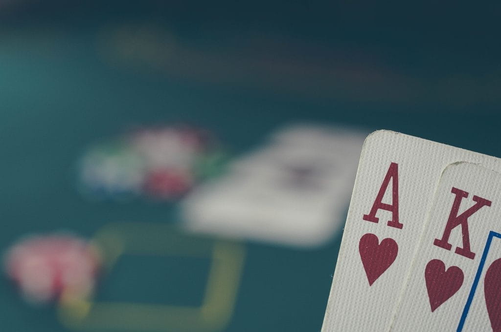  Die Pokerkarten Ass Herz und König Herz werden vor einem Pokertisch gehalten.