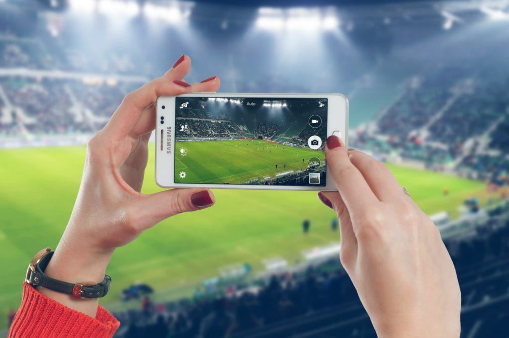 Eine Frau im Stadion filmt mit dem Smartphone ein Fußballspiel.