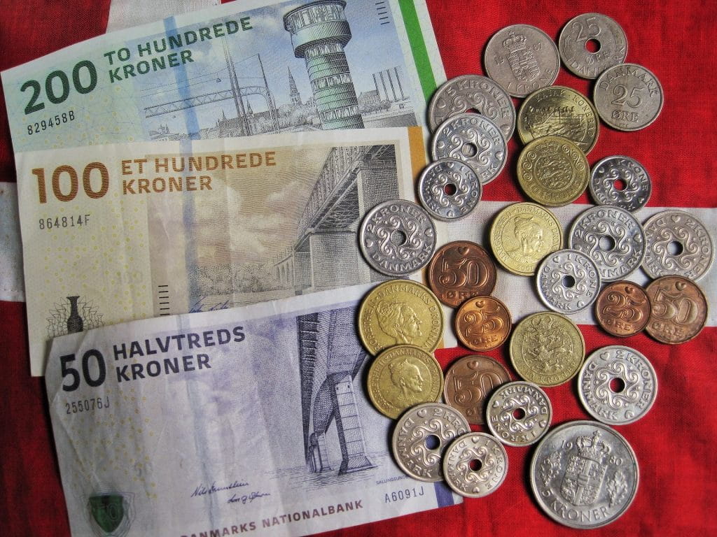 Dänisches Geld (Kronen) mit verschiedenen Münzen und Scheinen auf rotem Tischtuch liegend.