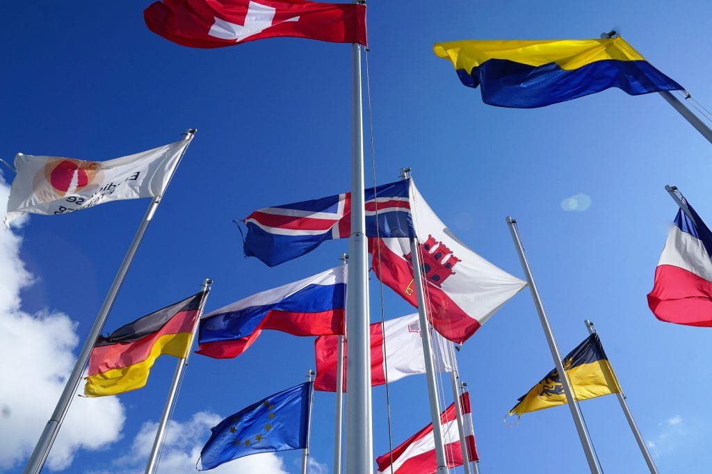 Flaggen von Ländern aus aller Welt im Wind unter blauem Himmel.