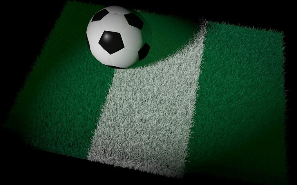 Fußball liegt auf nigerianischer Flagge, die auf Rasenfläche gemalt ist.