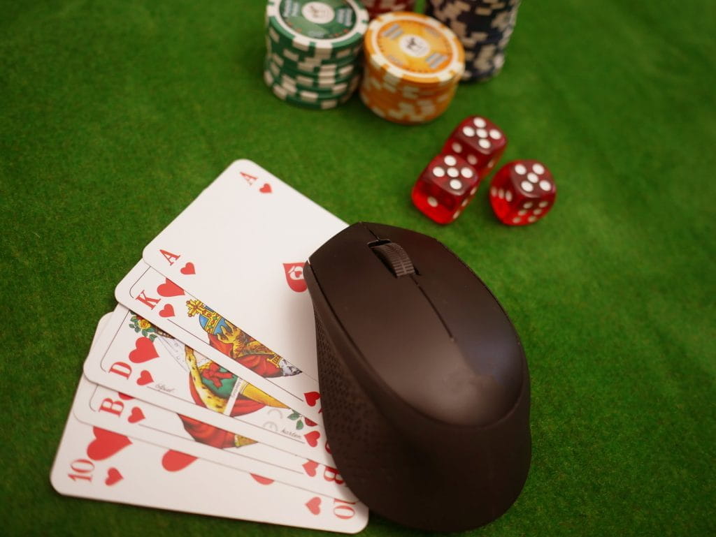 Auf einem Pokertisch liegen Pokerchips, Würfel, Spielkarten und eine Computermaus.