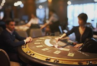 Weiblicher Croupier gibt Karten an Spieler an Blackjack-Tisch.