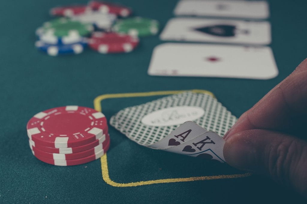Auf einem Pokertisch liegen Pokerchips und eine Hand hebt zwei Spielkarten ein kleines Stück hoch.