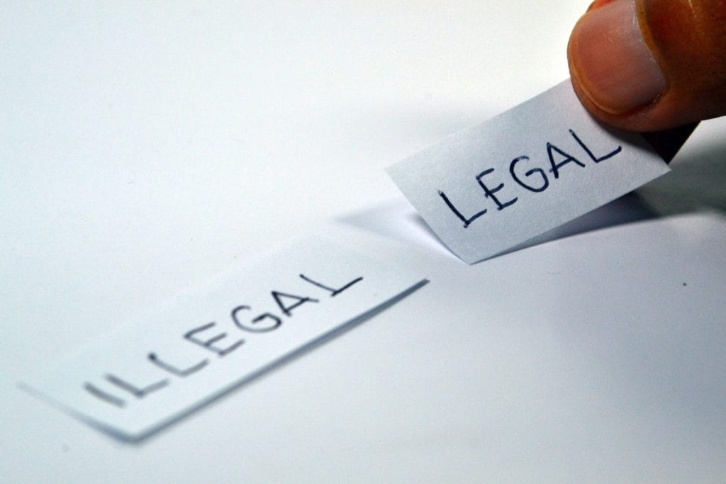 Finger legt Zettel mit Aufschrift LEGAL auf weißen Untergrund rechts neben weiteres Schild mit Aufschrift ILLEGAL.