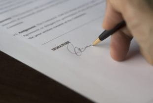 Eine Hand unterzeichnet mit einem Kugelschreiber einen Vertrag.