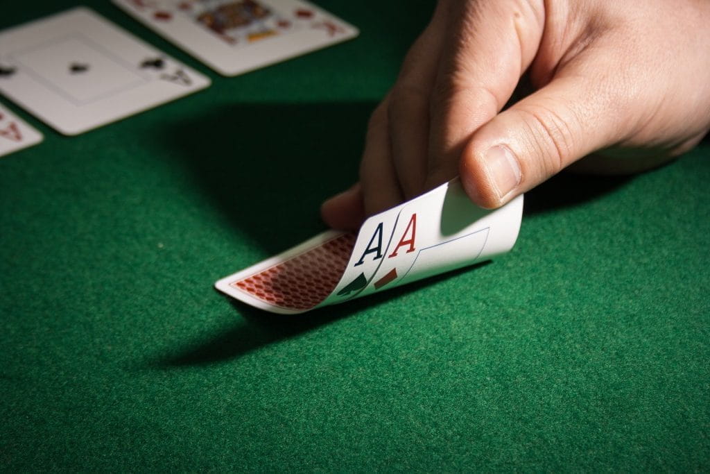 Eine Hand hebt zwei Ass-Spielkarten leicht an.