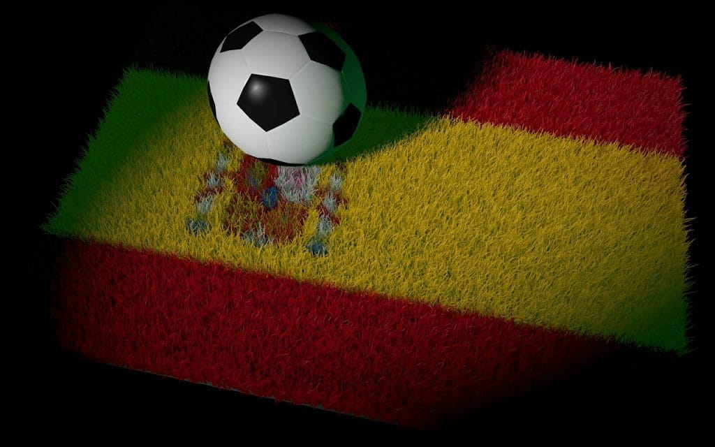 Animierter Fußball im klassischen Design liegt auf Rasen in Optik der spanischen Nationalflagge.