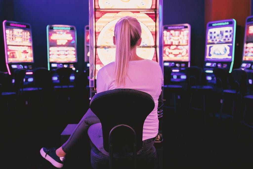 Blonde junge Frau sitzt vor Spielautomaten.