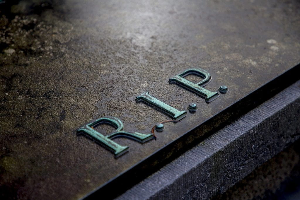 Ein dunkler Grabstein in der Nahaufnahme mit der Aufschrift R.I.P.