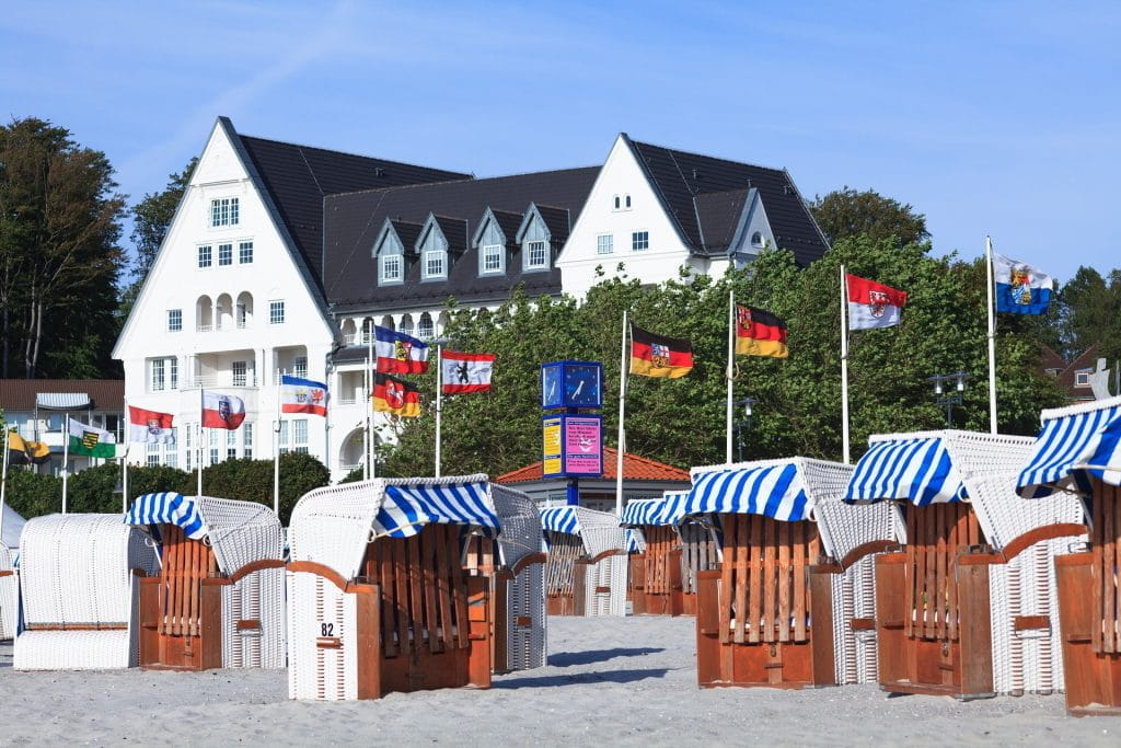 Fahnen der deutschen Bundesländer nebeneinander an einem Strand; im Vordergrund Strandkörbe.