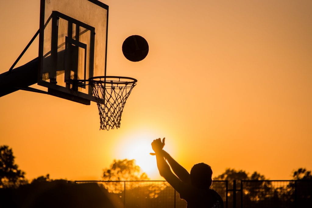 Sportler wirft Basketball in Richtung Korb vor Sonnenuntergang.