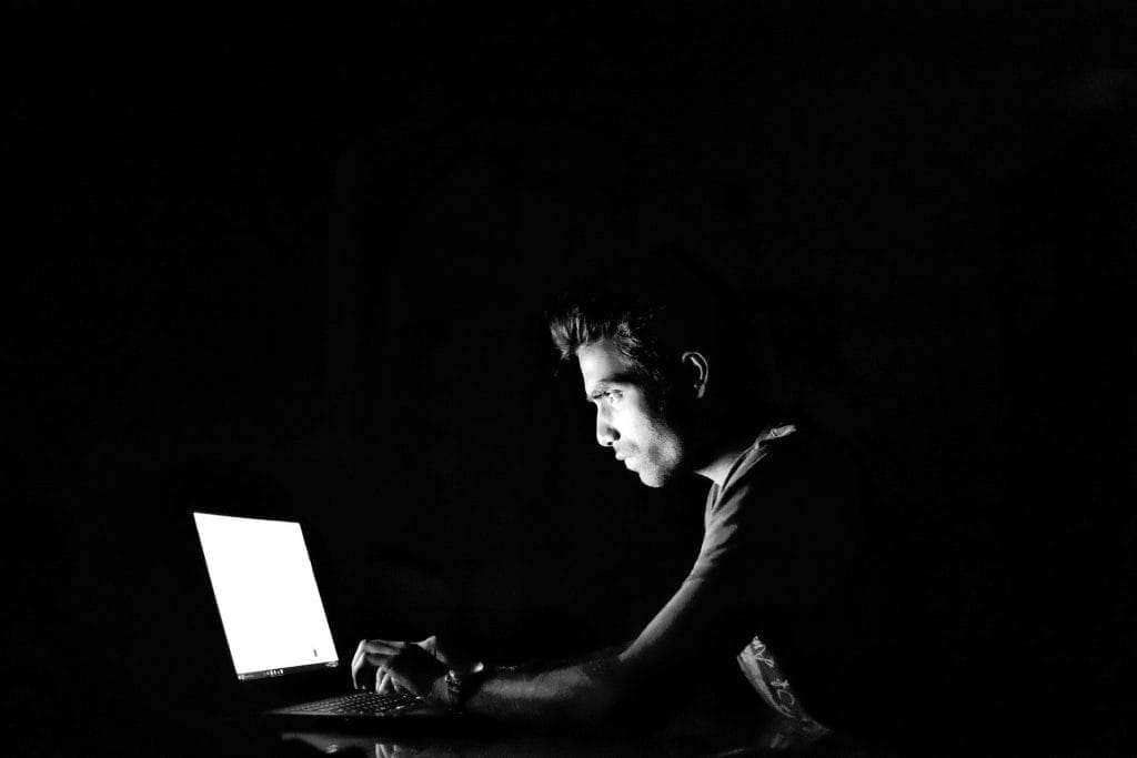 Ein Mann sitzt in einem dunklen Raum vor einem Laptop.