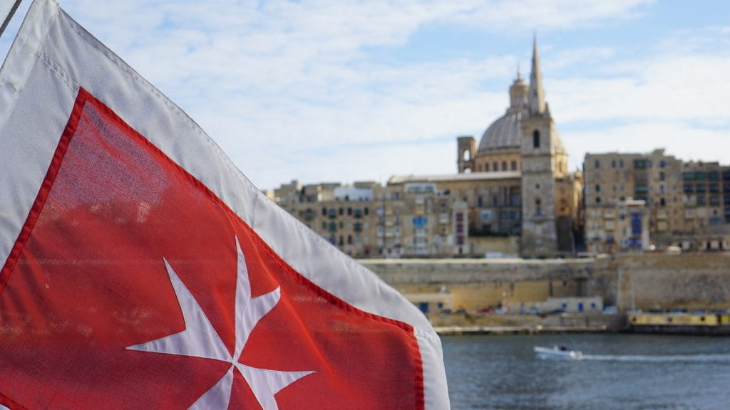Die Flagge von Malta und eine Stadt im Hintergrund.