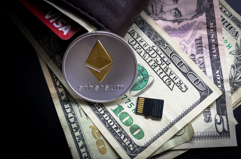 Münze der Kryptowährung Ethereum lehnt an ein Portemonnaie mit Dollarscheinen.