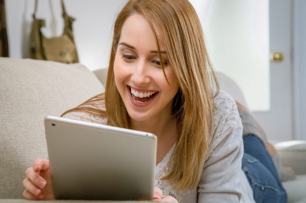 Eine Frau liegt auf Couch und zockt am Tablet.