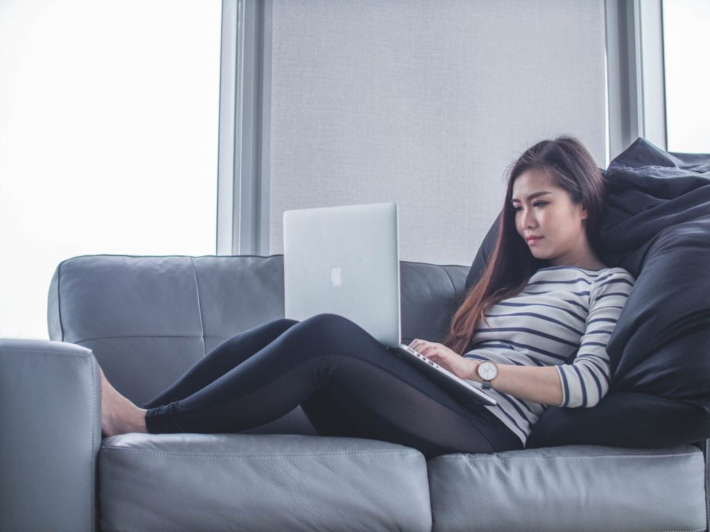Eine Frau liegt mit einem Laptop auf der Couch.