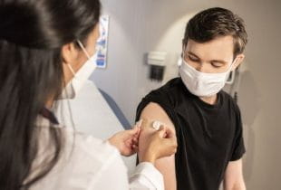 Eine Ärztin klebt einem Patienten nach einer Impfung ein Pflaster auf den Oberarm.