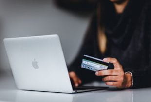 Eine Frau am Laptop hält eine Kreditkarte in linker Hand.