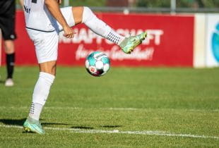 Ein Fußballer hält einen Ball hoch.