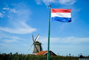 Die Flagge der Niederlande an einem Fahnenmast mit einer Windmühle im Hintergrund.