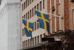 Zwei Fahnenmasten an einer Hausfassade mit der schwedischen Nationalflagge.