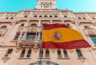 Spanische Flagge am Fahnenmast vor Gebäudefassade.