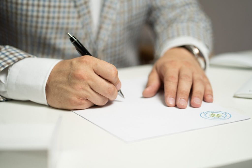Eine Person im Anzug unterschreibt ein Dokument mit einem Kugelschreiber.