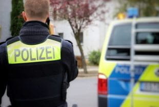 Ein Polizeibeamter steht vor einem Polizeiwagen und telefoniert.