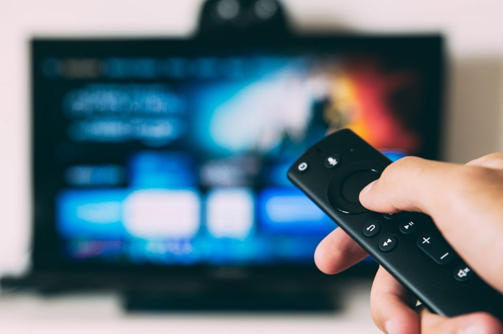 Eine Person startet einen Stream mit einer Fernbedienung auf einem TV-Gerät.