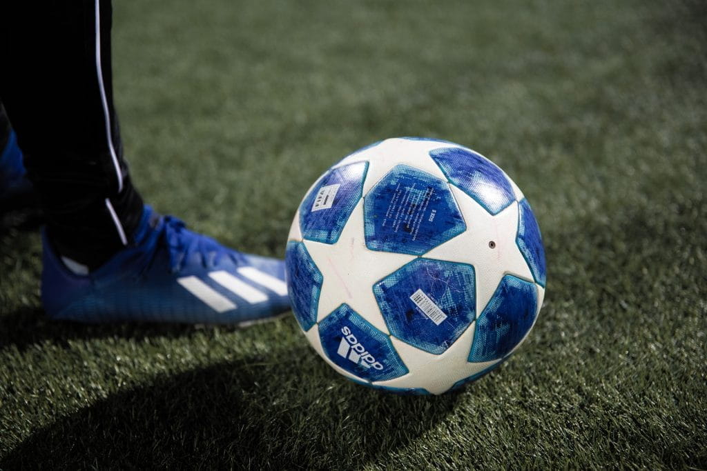 Eine Person steht auf einem Rasen neben einem Fußball.