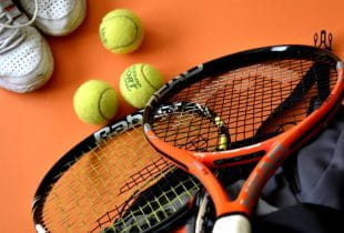 Eine Tasche, Sportschuhe sowie Tennisbälle und -schläger auf orangenem Untergrund.