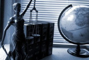 Die Statue der Göttin Justicia, ein Globus und Gesetzesbücher auf einem Schreibtisch.