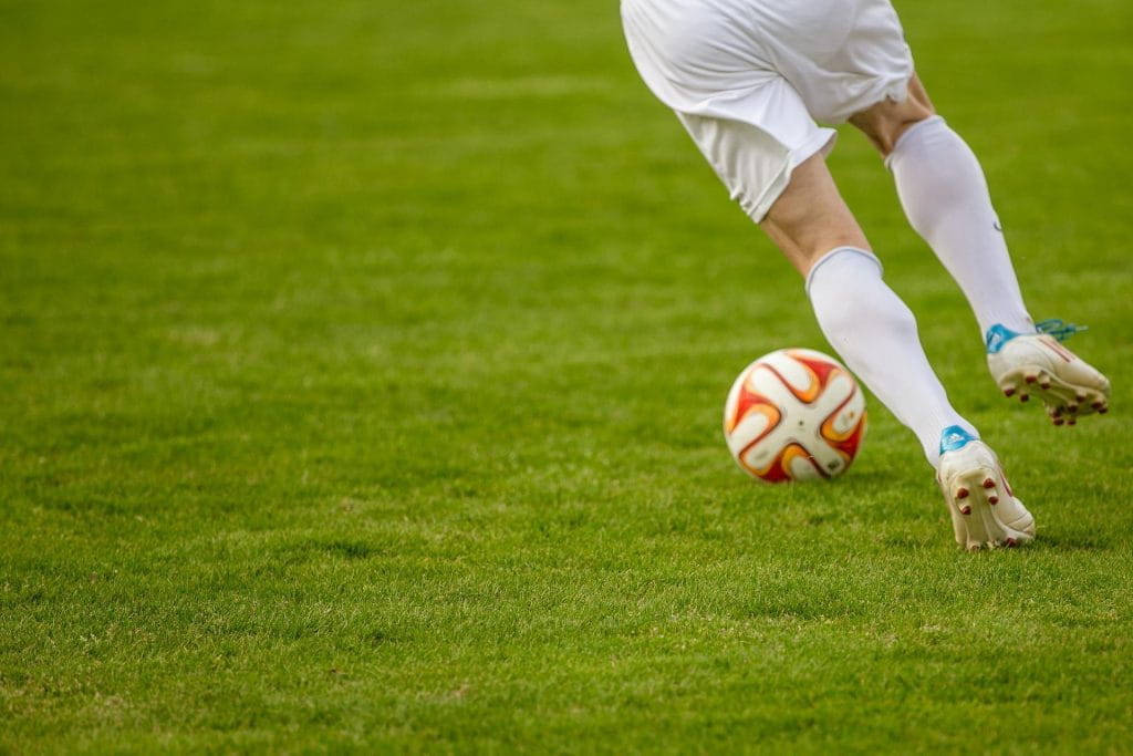 Ein Fußballspieler mit einem Ball auf grünem Rasen.