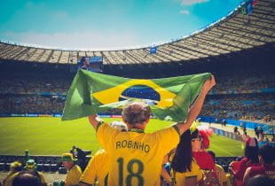 Ein Mann mit Brasilen-Trikot und -Fahne in einem Fußballstadion.