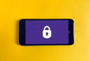 Smartphone auf senfgelbem Hintergrund mit einem Schlosssymbol auf dem Display.