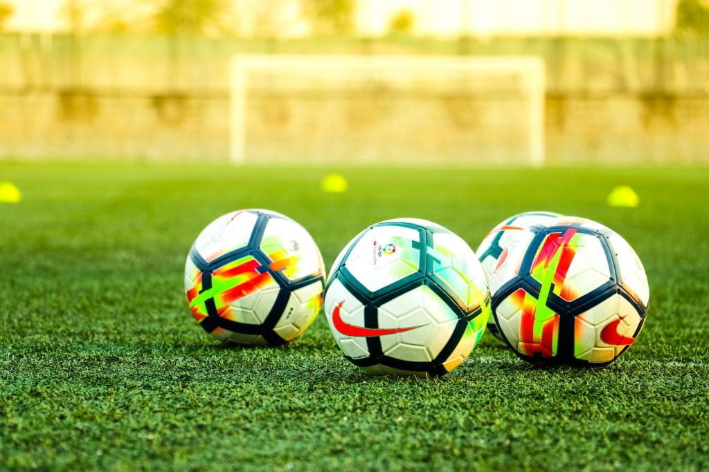 Empat bola sepak di rumput sintetis.
