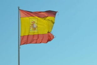 Die Flagge Spaniens weht am Fahnenmast vor strahlend blauem Himmel.