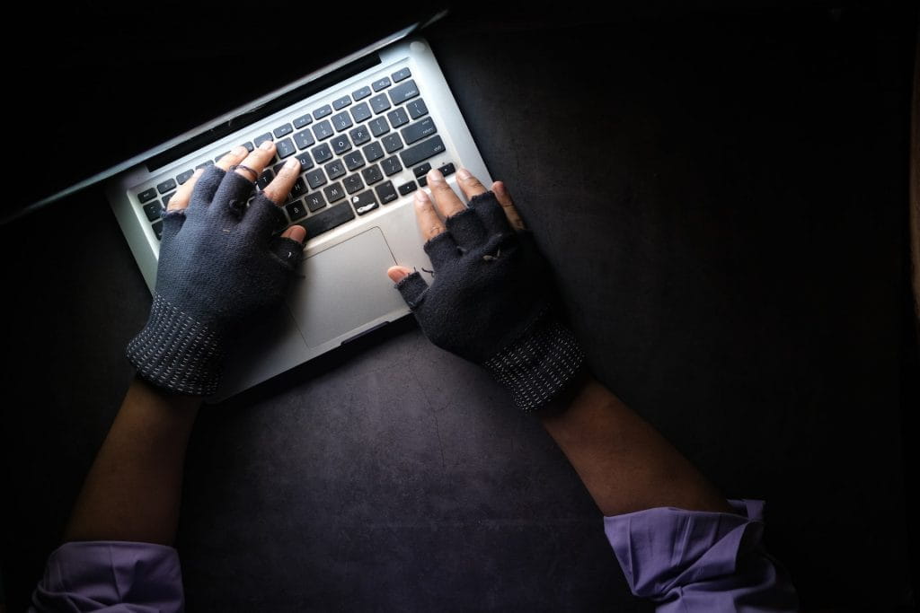 Seorang penjahat yang memakai sarung tangan sedang mengetik di MacBook.