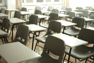 Ein Klassenzimmer in einer Schule mit sauber aneinandergereihten Tischen und Stühlen.