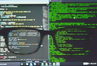 Codierungen auf zwei Displays mit einer verschwommenen Brille im Vordergrund.