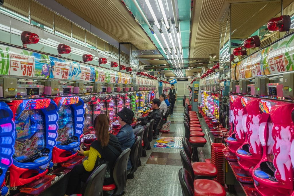 Beberapa orang sedang duduk di depan mesin slot di arcade Jepang.