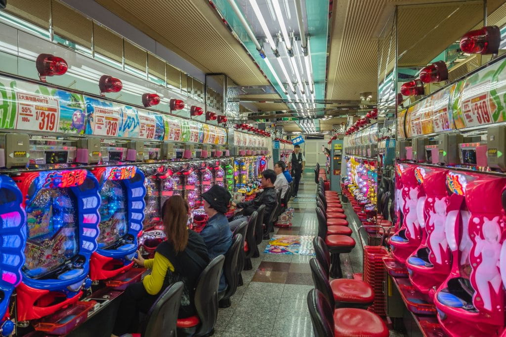 Mehrere Menschen sitzen an Spielautomaten in einer japanischen Spielhalle.