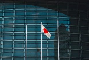Die japanische Nationalflagge hängt an einem Fahnenmast vor einer gläsernen Gebäudefront.