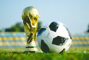 Der WM-Pokal und der WM-Ball auf einem Rasenfußballfeld.