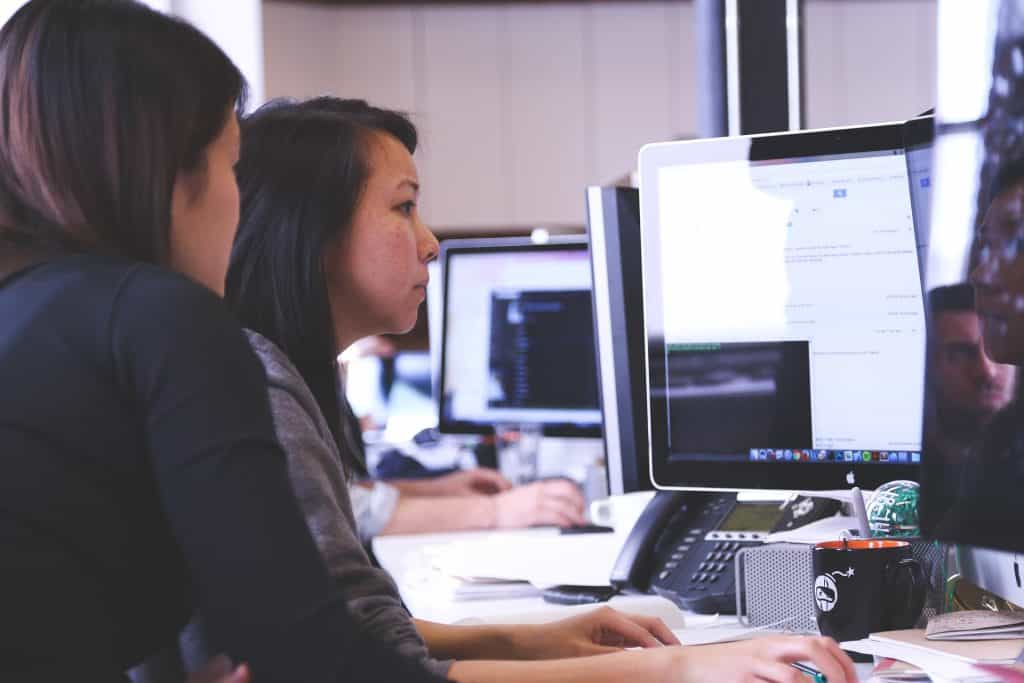 Dua wanita sedang duduk di depan komputer di kantor dan sedang bekerja