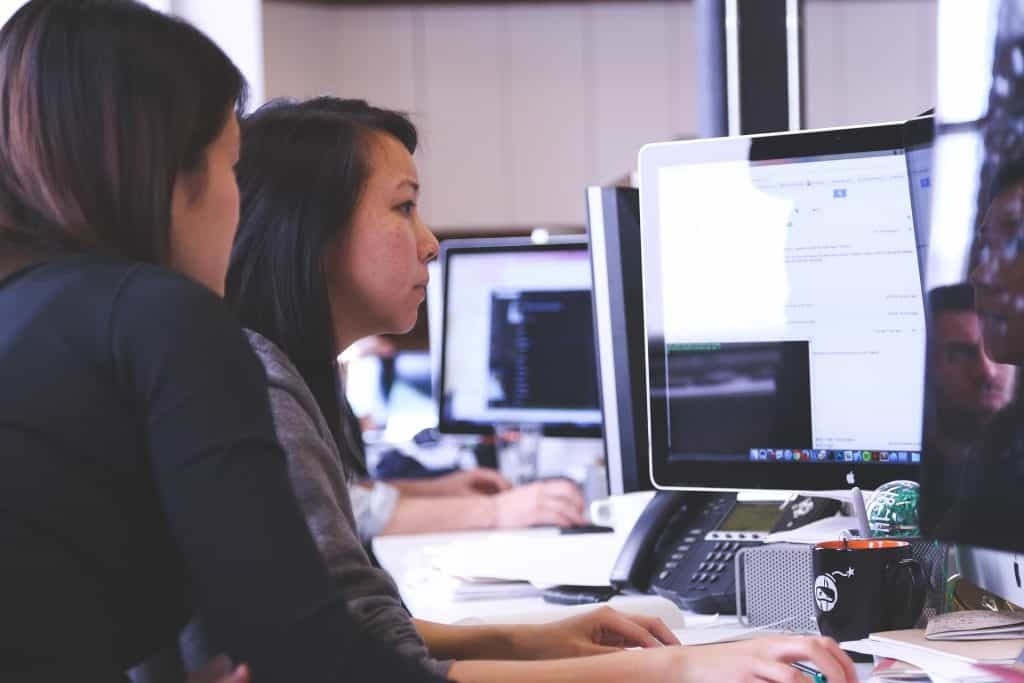 Zwei Frauen sitzen in einem Büro vor einem Computer und arbeiten